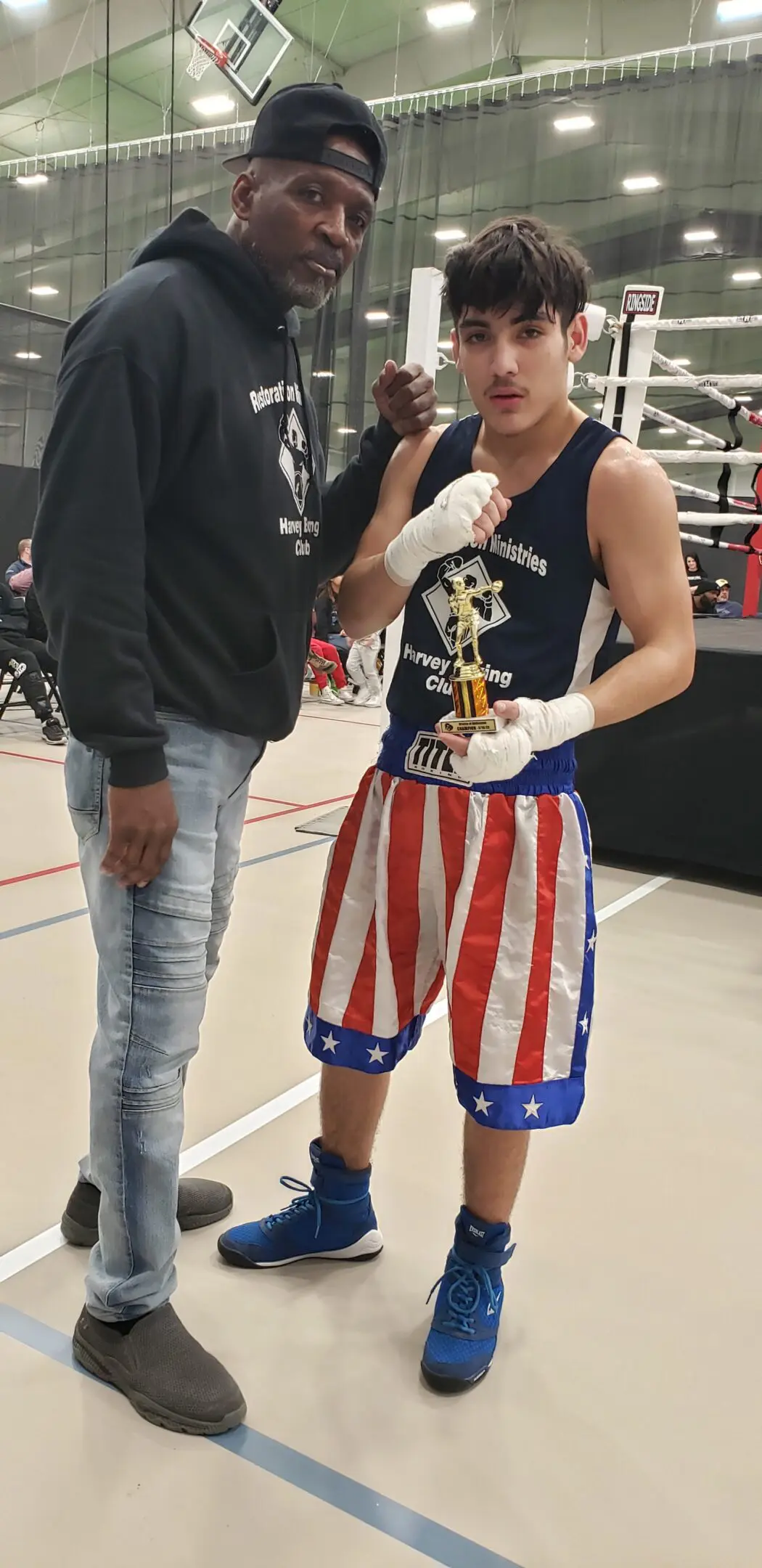 Boxer posing in patriotic red, white, and blue boxing shorts with a man beside him.