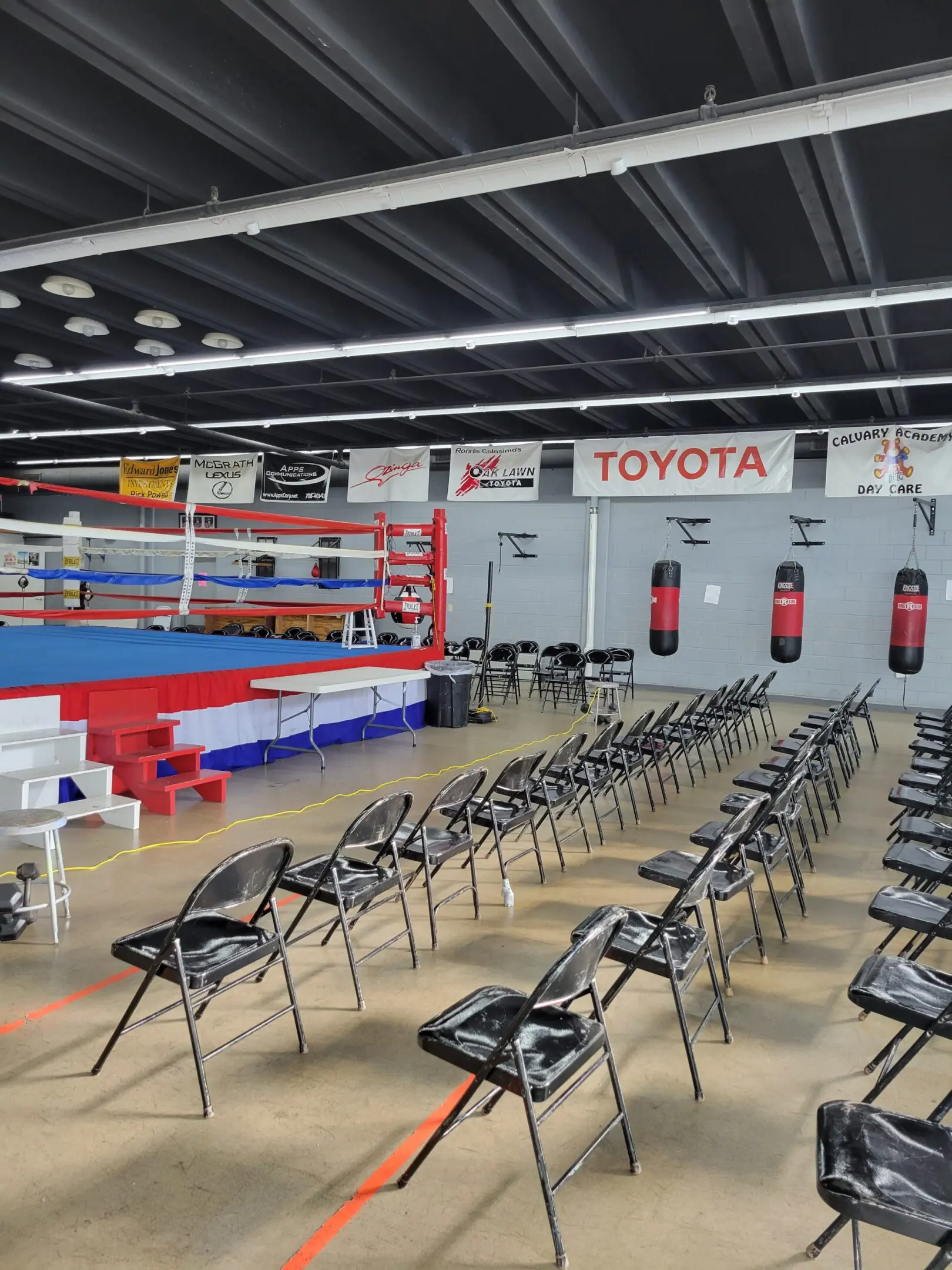 Indoor boxing gym with ring, chairs, and punching bags under Toyota banners.